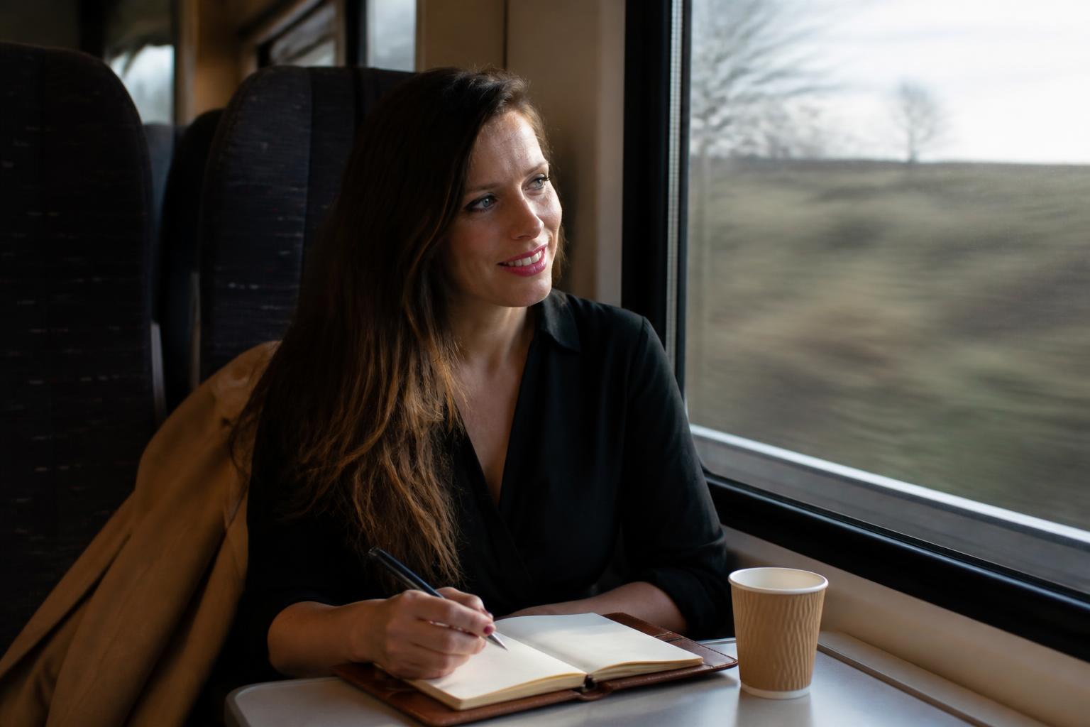 Amélie Huygens kijkt uit het raam van de trein, met notitieboek en koffie